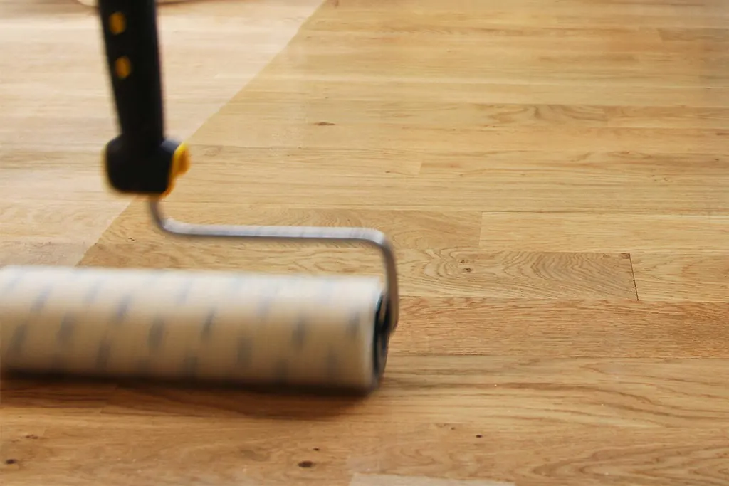 Un rouleau applique une finition sur un parquet en chêne