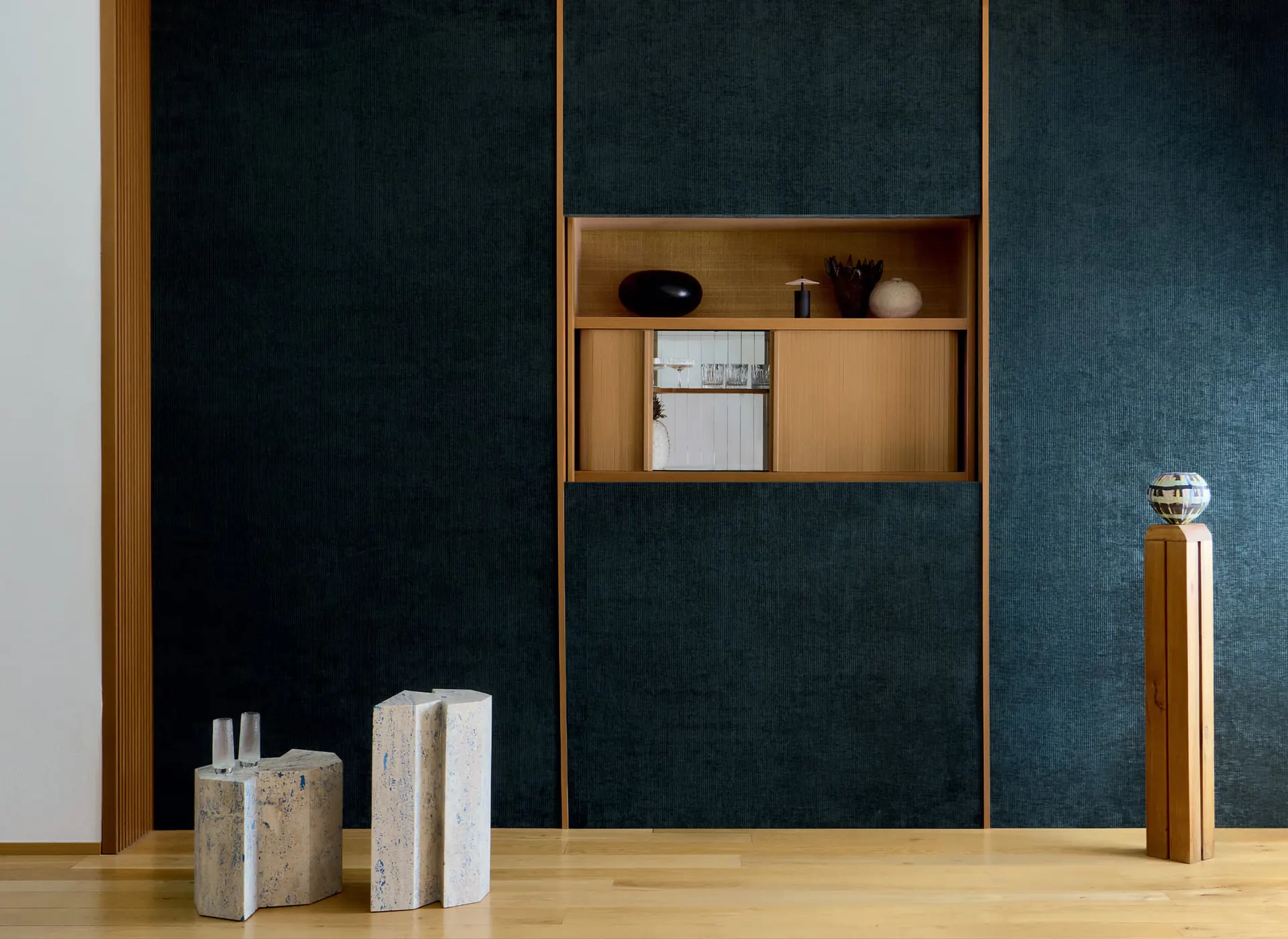 Mur bleu nuit tissé, niche en bois clair et sculptures