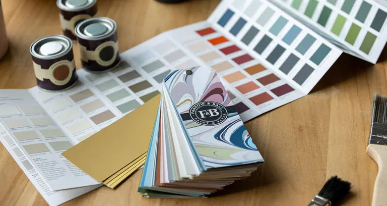 Nuancier Farrow & Ball déplié à côté de petits pots de peinture et d'un pinceau